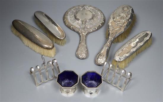 A silver mounted mirror, four silver brushes, a pair of toastracks and a pair of silver salts.